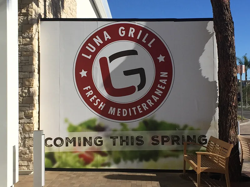 The Luna Grill badge printed at wall scale on a construction barricade, above the words coming this spring
