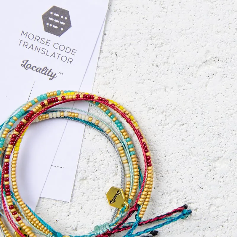 A stack of handmade Locality morse code bead bracelets in muted, earthy tones.
