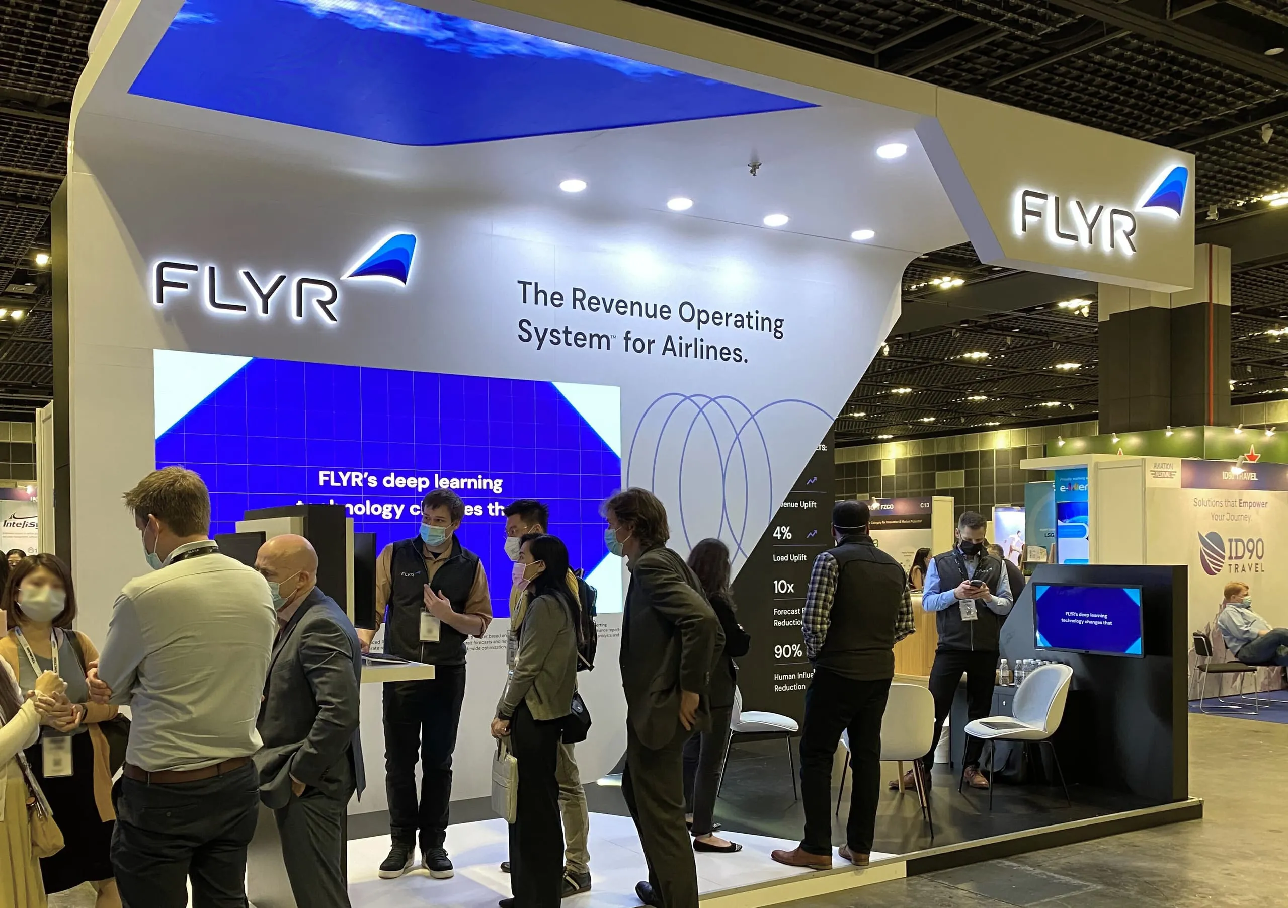 Attendees standing several deep at the LED wall while it runs a deep learning message, the sky panel lit in the ceiling above the stand.