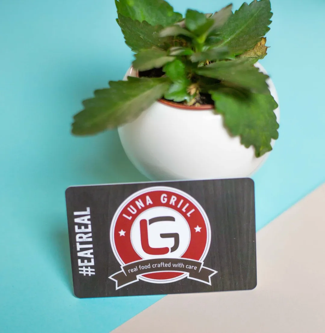 A Luna Grill gift card carrying the monogram badge and the brand promise on a ribbon
