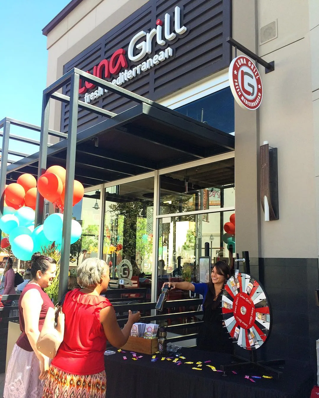 A grand opening with balloons outside a Luna Grill, the fresh mediterranean descriptor on the channel letter sign and the badge on a blade sign