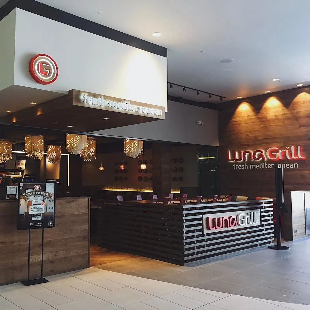 A mall storefront showing the badge on a blade sign, the wordmark on the wall, and the lockup at counter height