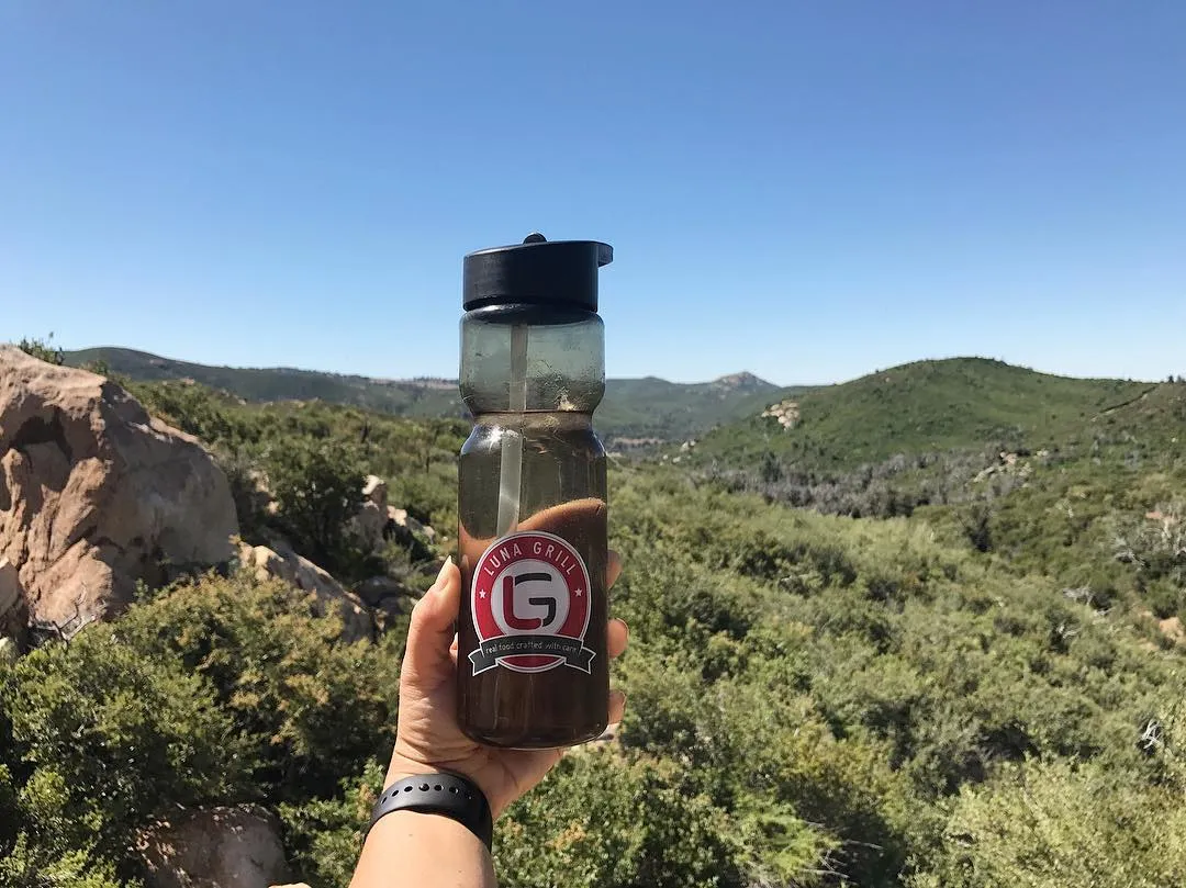 A branded water bottle held up on a hike